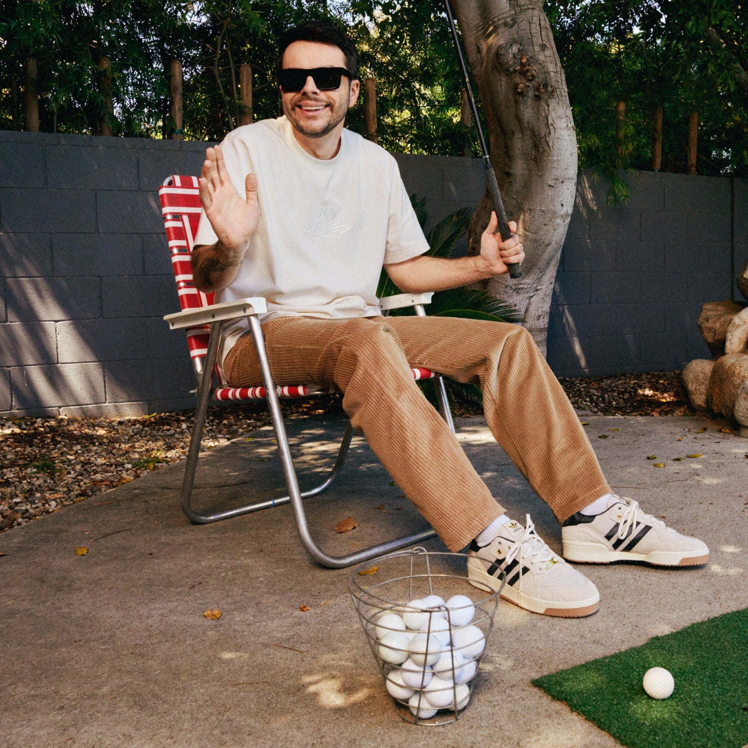 Nadeshot seated with a golf club, wearing adidas collaborative sneakers