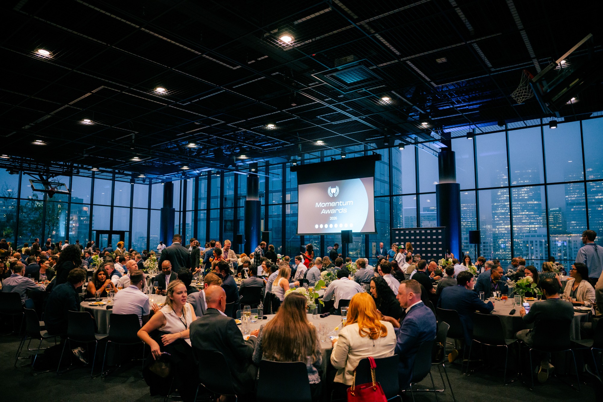 Attendees talking around tables beneath the screen at the 2026 Momentum Awards