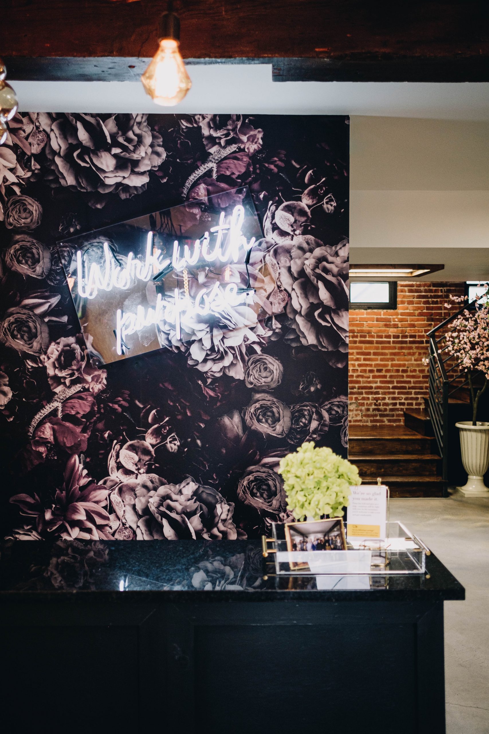 The reception area at the 19 Ideas office, with floral wallpaper, exposed brick and a neon Work with purpose sign