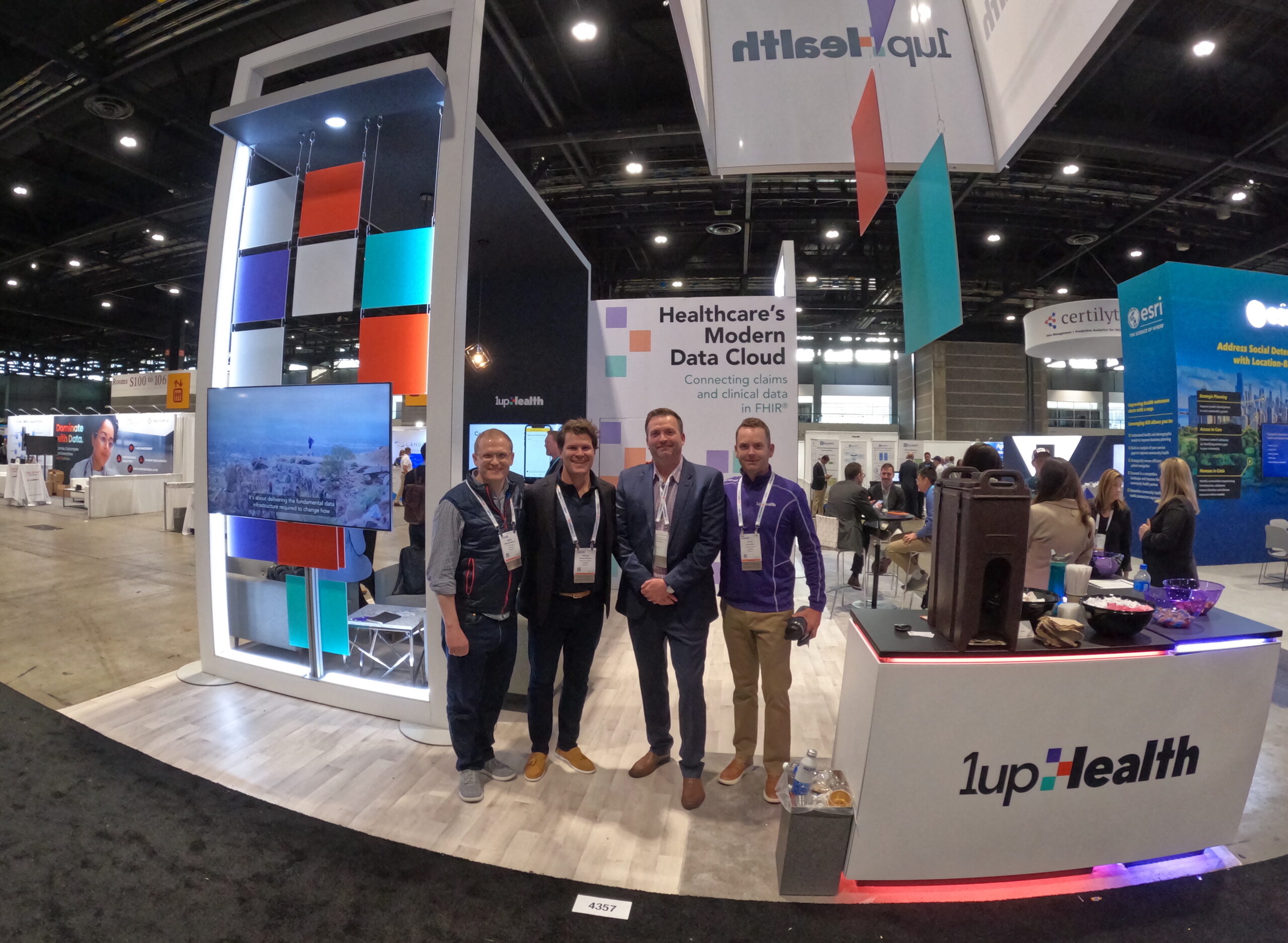 Four people standing at a 1upHealth exhibition booth