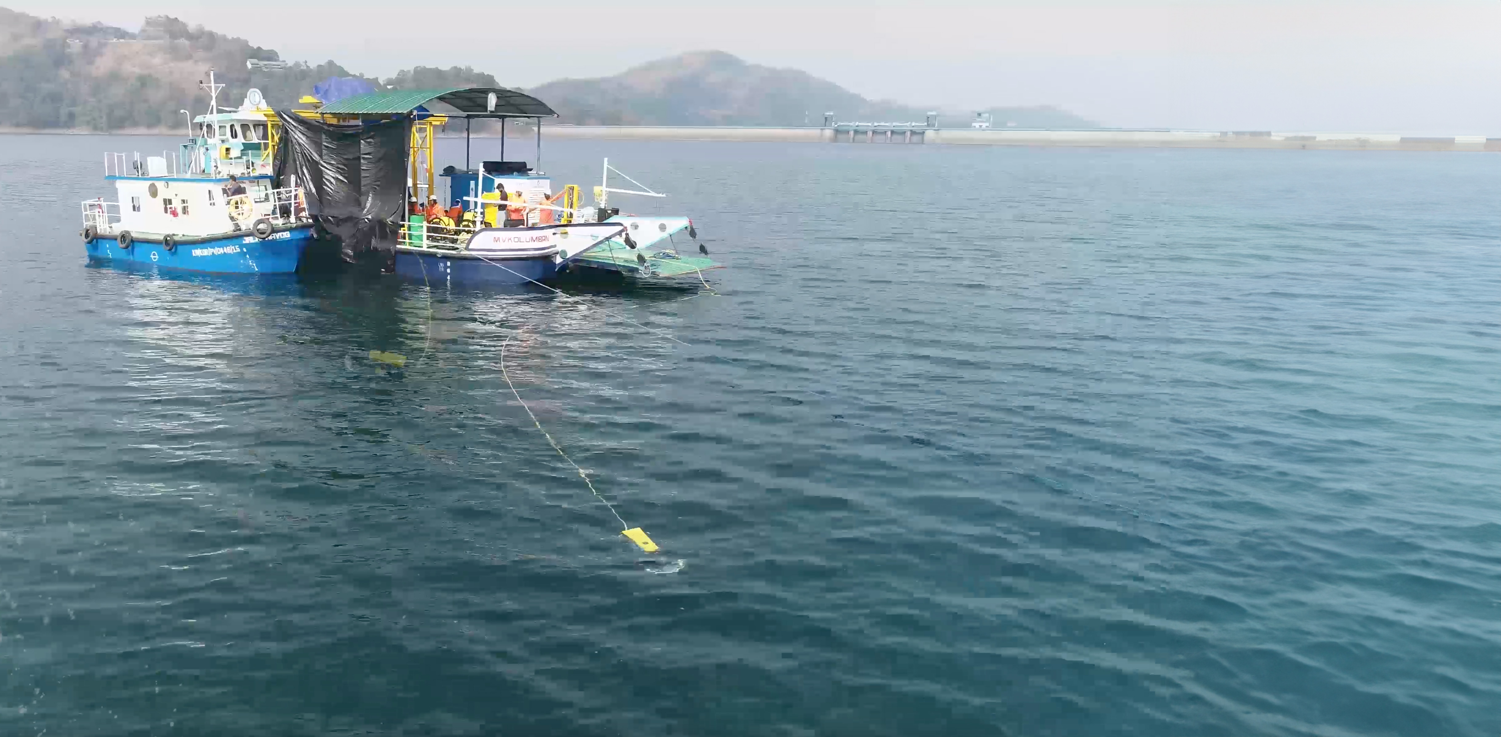 A tethered yellow Planys inspection robot in the water beside a workboat