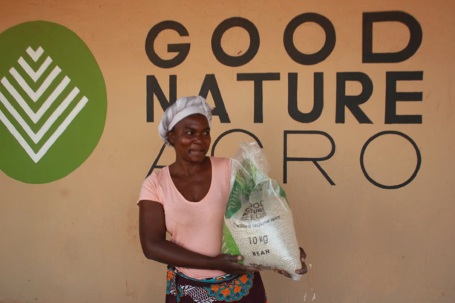 A woman holding a bag of seed in front of Good Nature Agro signage