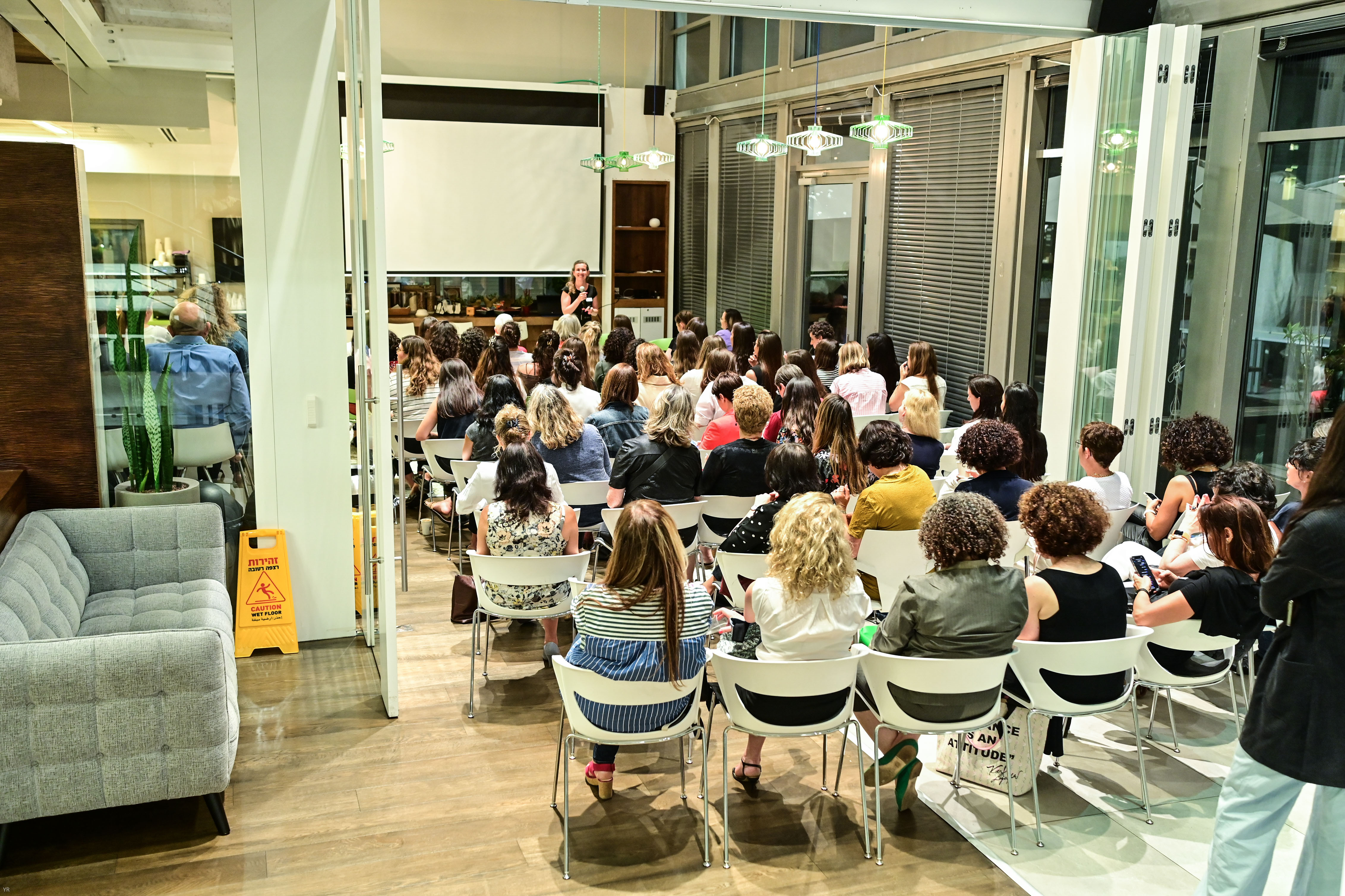 An audience seated in a glass-walled room listening to a speaker at an association event