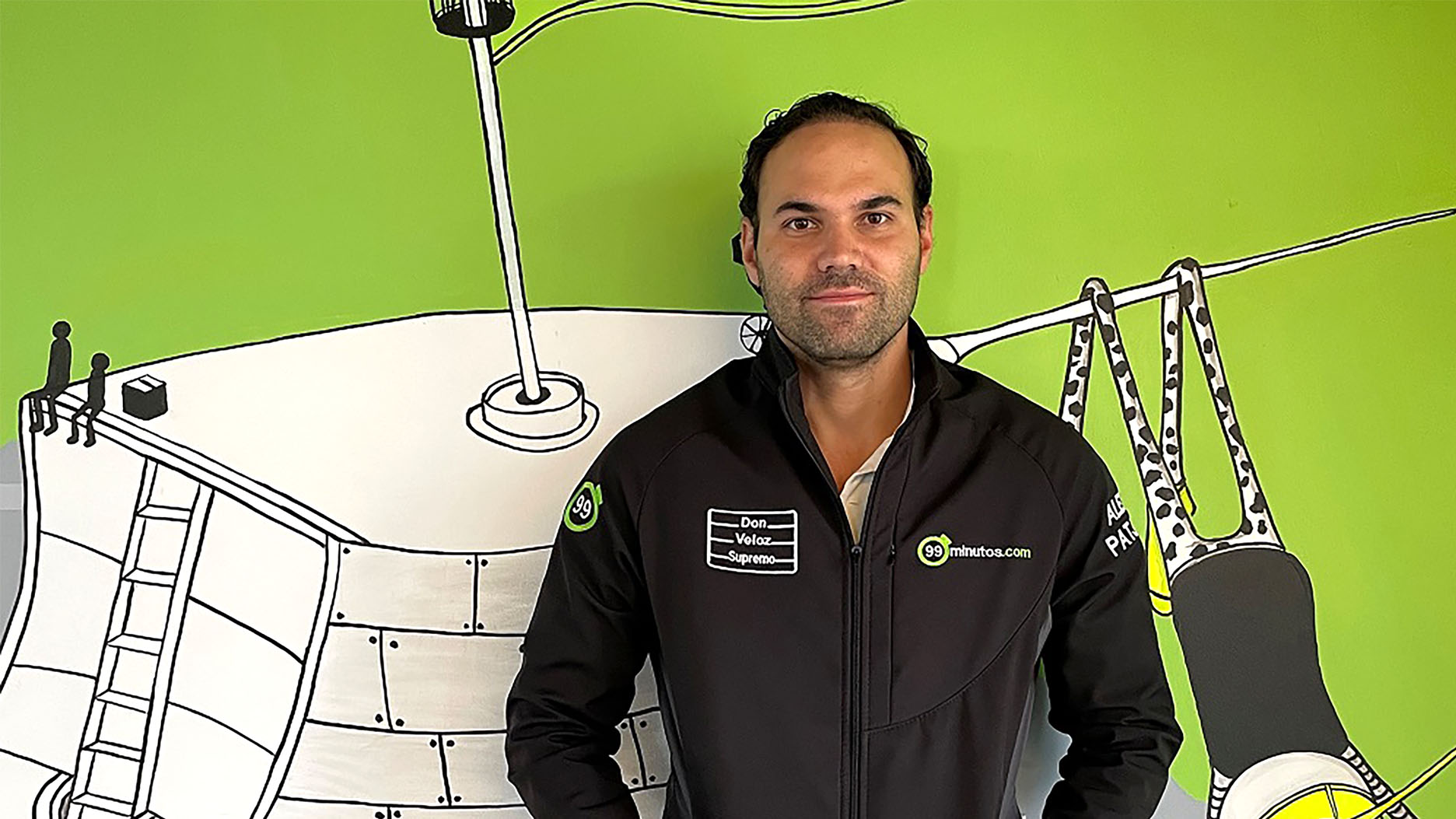 99minutos founder Alexis Patjane wearing a company jacket in front of a green illustrated wall