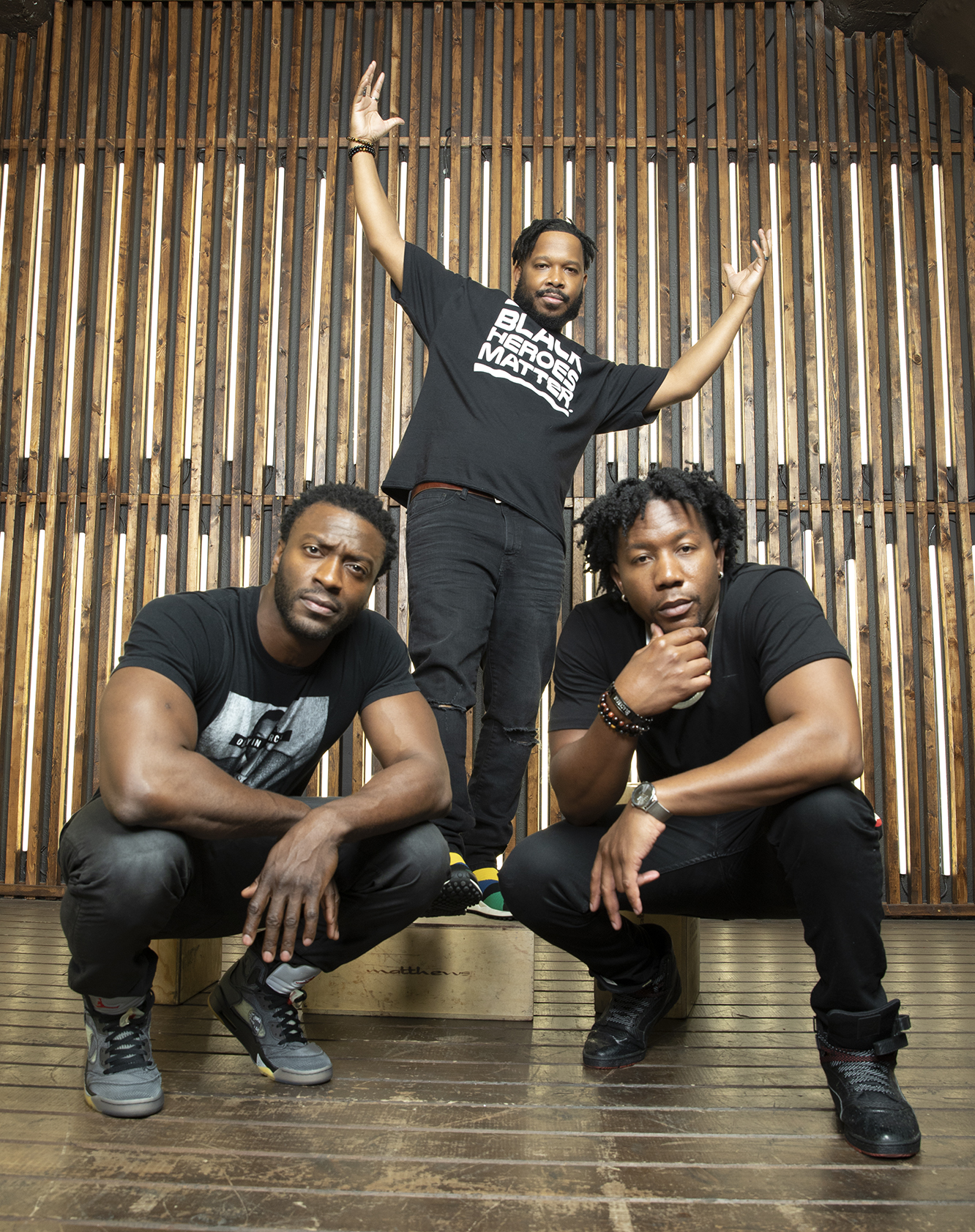 The three 9B Collective founders pose together against a wall of vertical wooden slats.