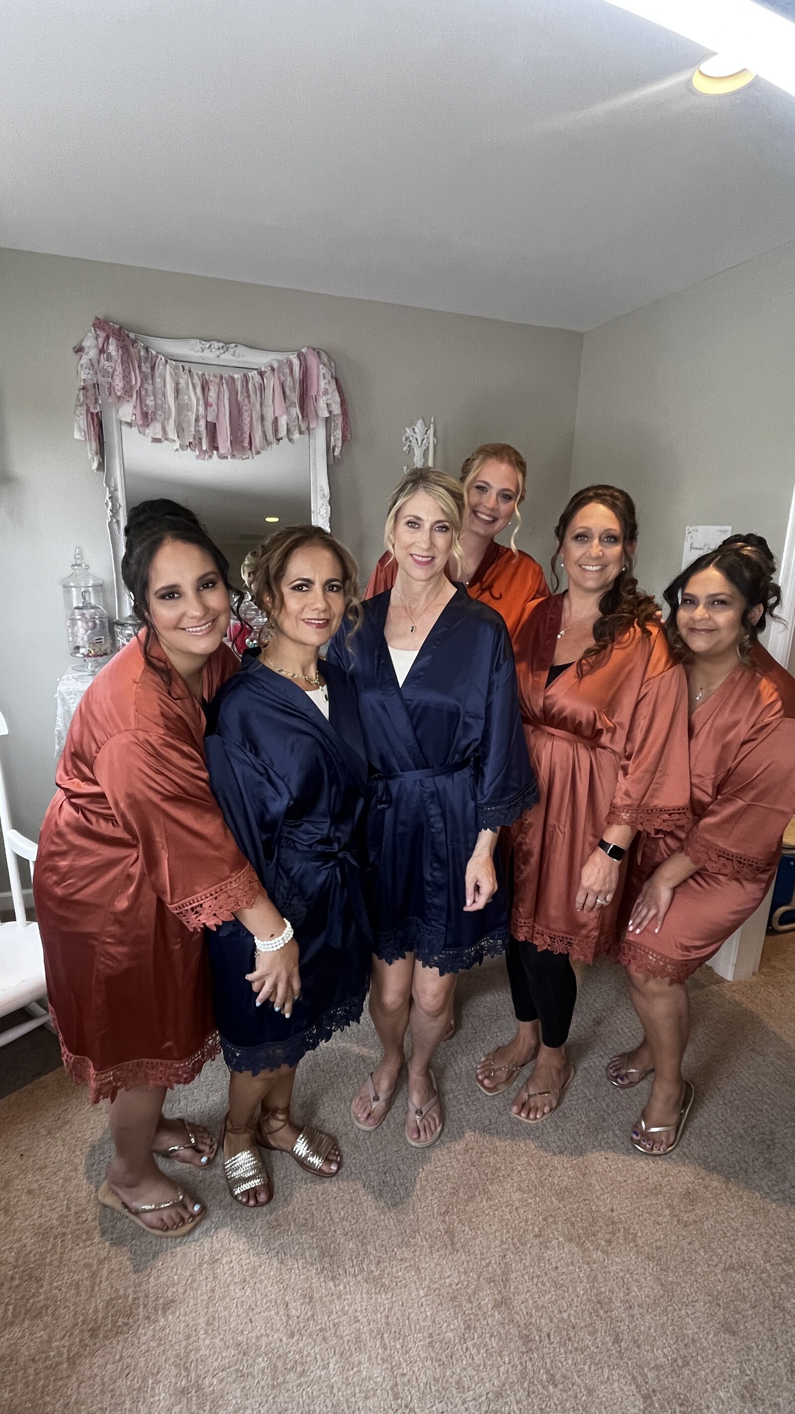 Six members of a bridal party in navy and rust robes pose together in the Love Loft