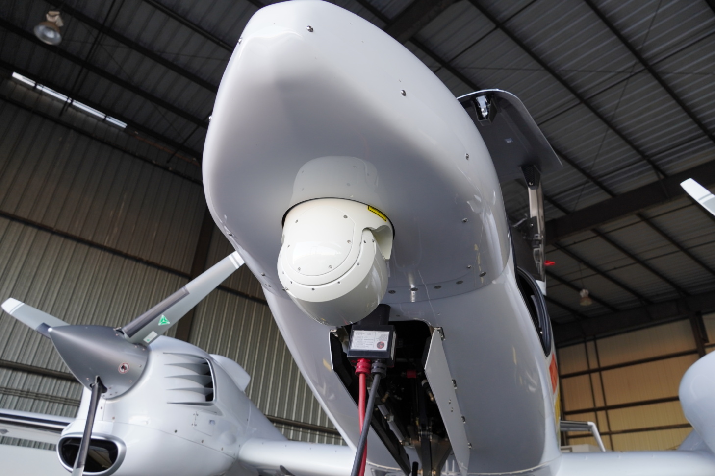 Aalyria Tightbeam laser terminal mounted beneath an aircraft in a hangar
