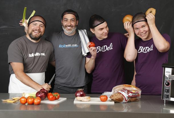Valentino Volonghi, Aaron Bell, Ville Tuulos and Jyri Tuulos in backward caps beside a counter of vegetables and bread