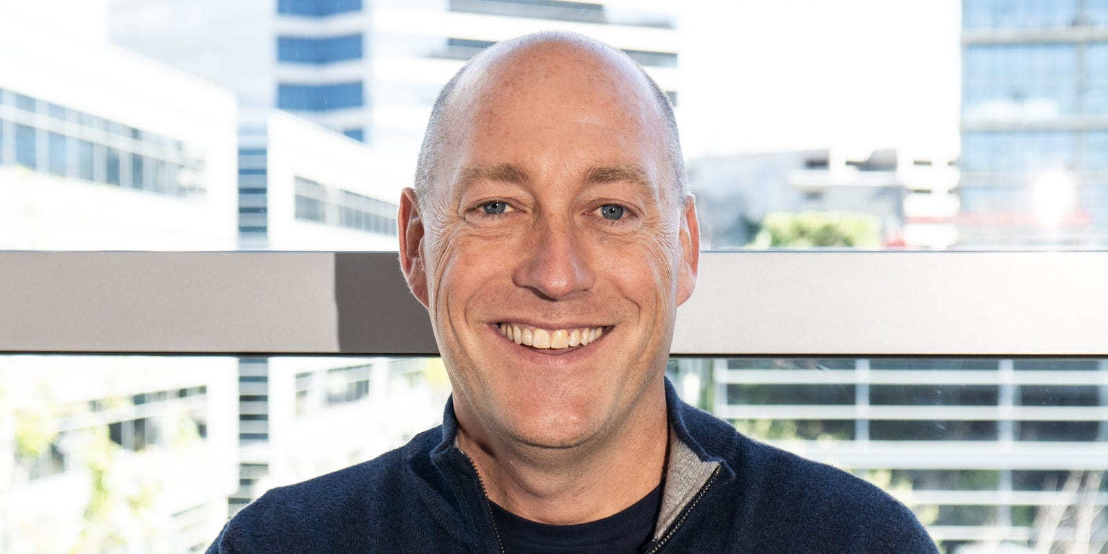 Aaron DeBevoise smiling in a bright office with buildings visible through the window
