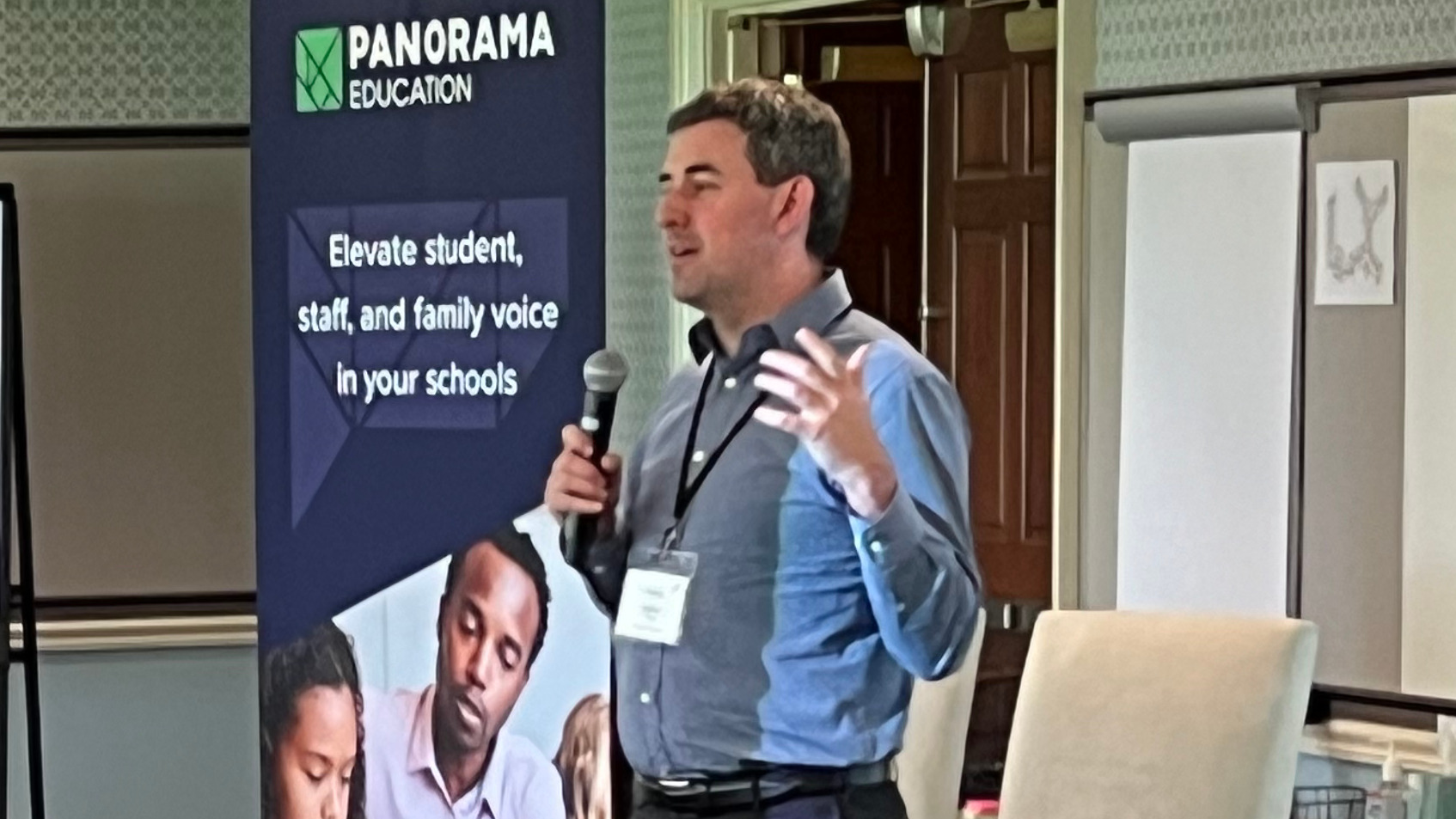 Aaron Feuer speaking with a handheld microphone beside a Panorama Education banner