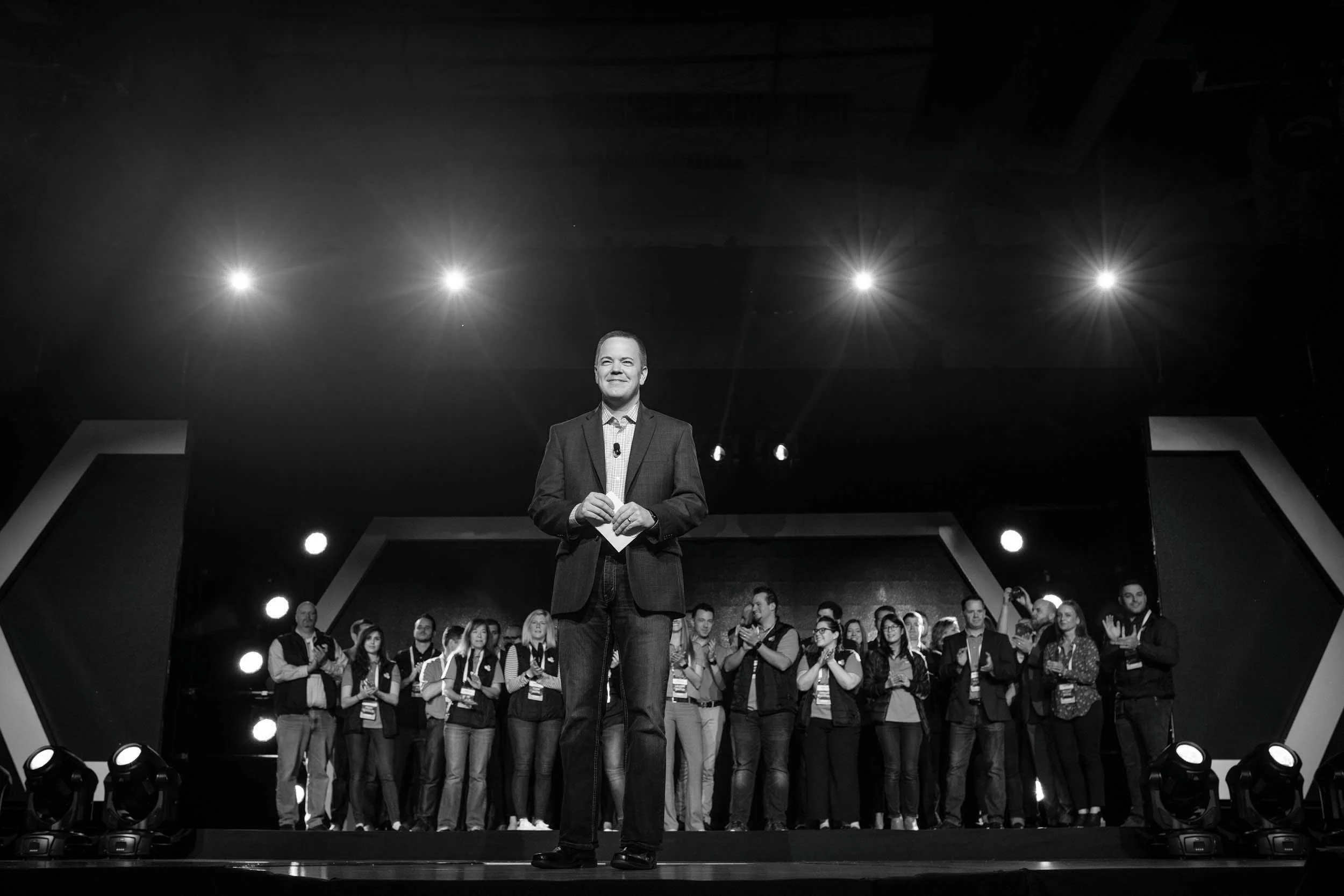 Aaron Klein speaking on a dark stage under spotlights