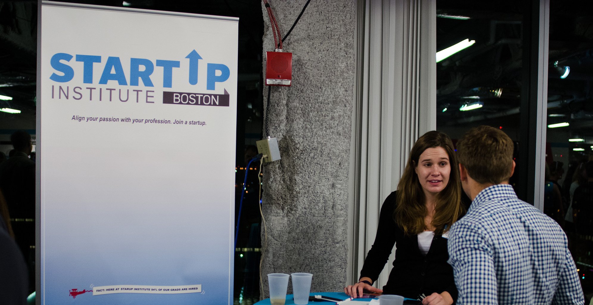 A conversation beside a Startup Institute Boston banner at an event