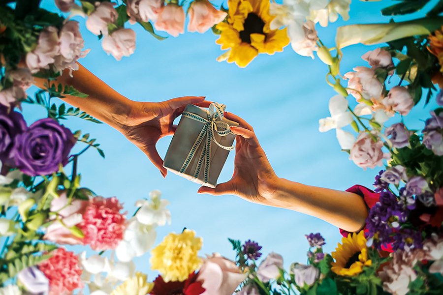 A wrapped gift passed between two hands, surrounded by flowers