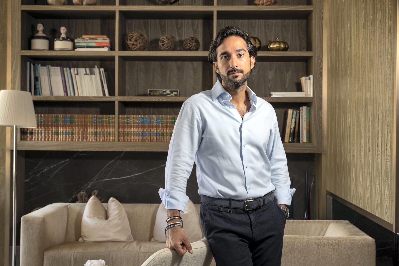 Abdulla Almoayed standing beside a sofa in front of bookshelves in Dubai
