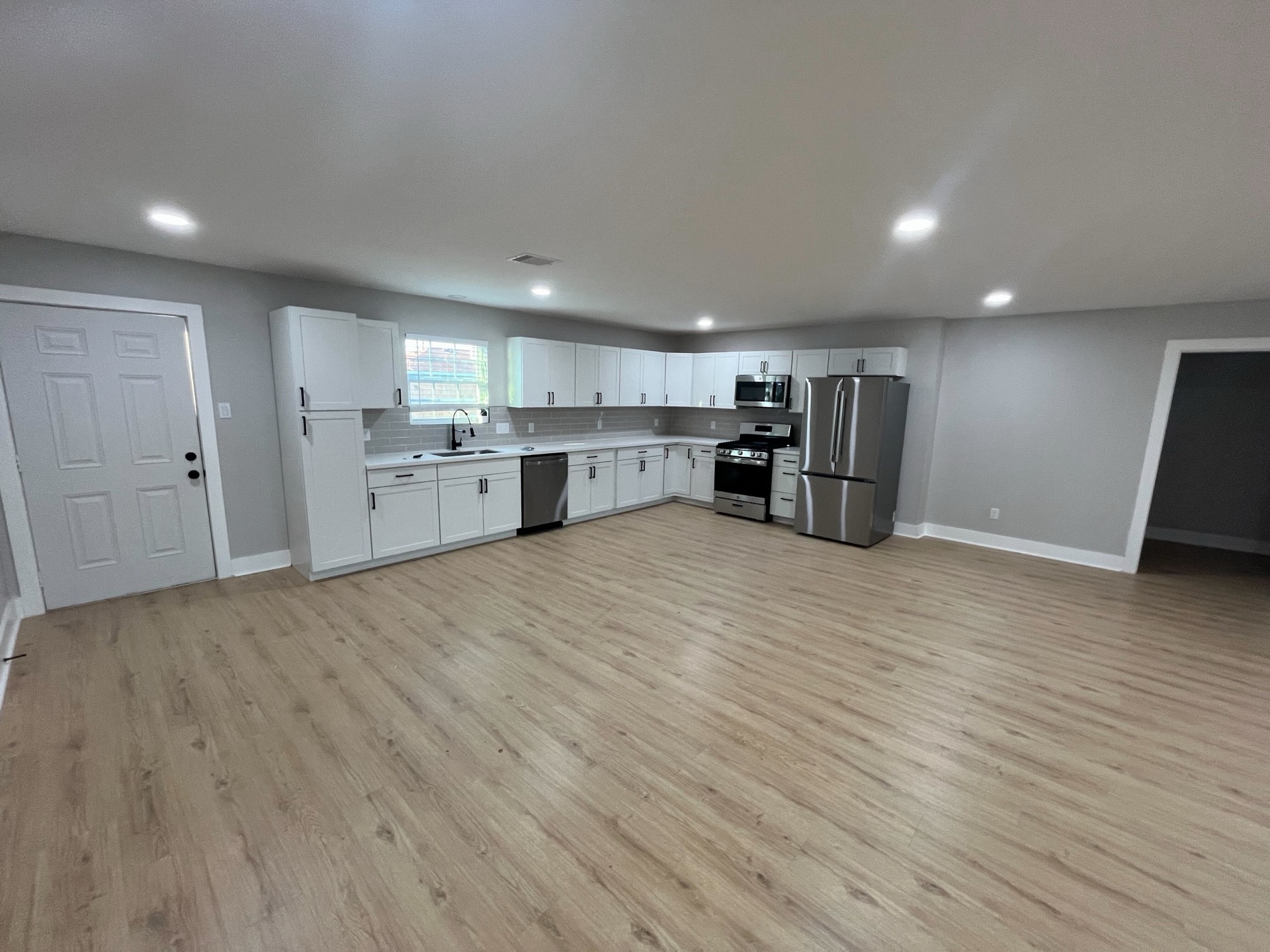 Renovated kitchen and living area in RentReady’s Houston restoration, with white cabinets and wood-look flooring