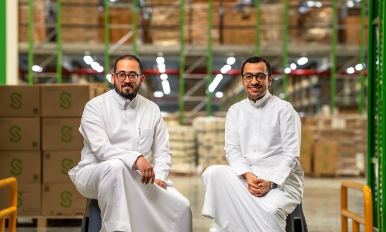 The two Salasa co-founders seated among shelves and cartons in a warehouse