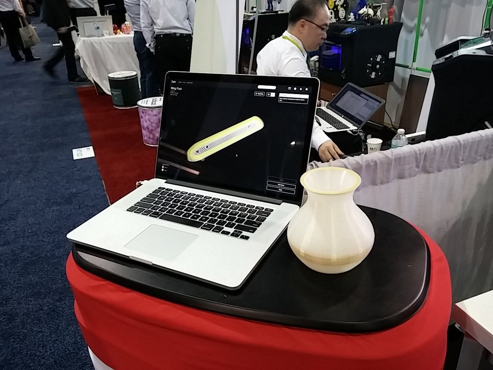 A laptop displaying Markforged Eiger software beside a printed vase at a trade-show demonstration