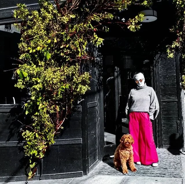 Abigail Kiefer wearing bright pink trousers while standing with her dog outside a dark-painted San Francisco building