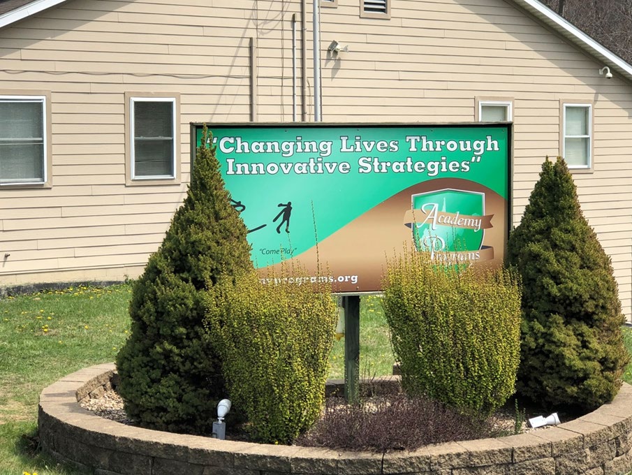 Academy Programs sign in front of a light-colored campus building