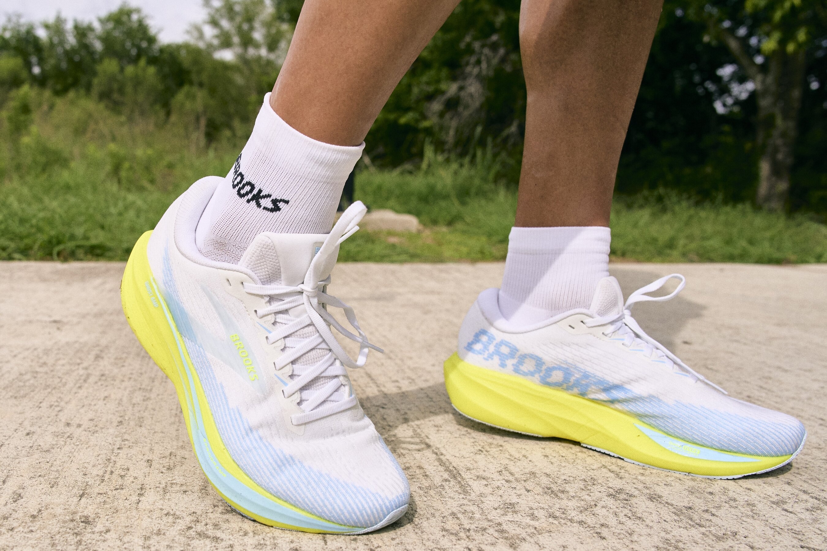 White Brooks running shoes with bright yellow soles on a runner’s feet outdoors