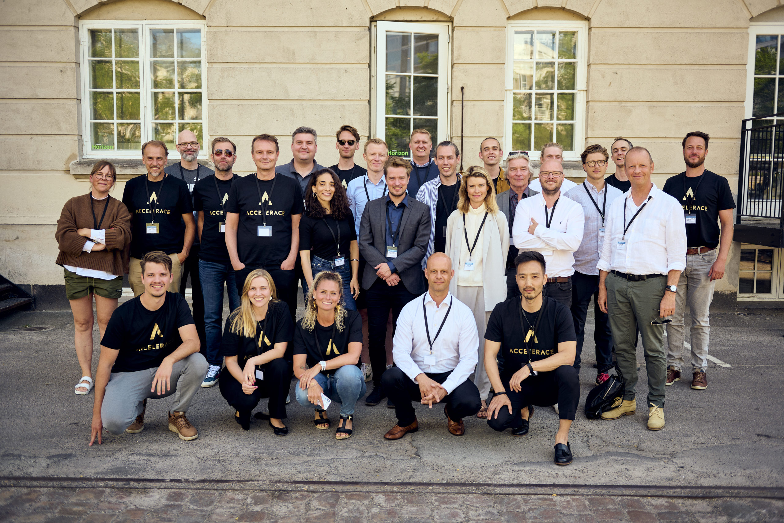An Accelerace community group poses outside a building, several wearing Accelerace T-shirts.