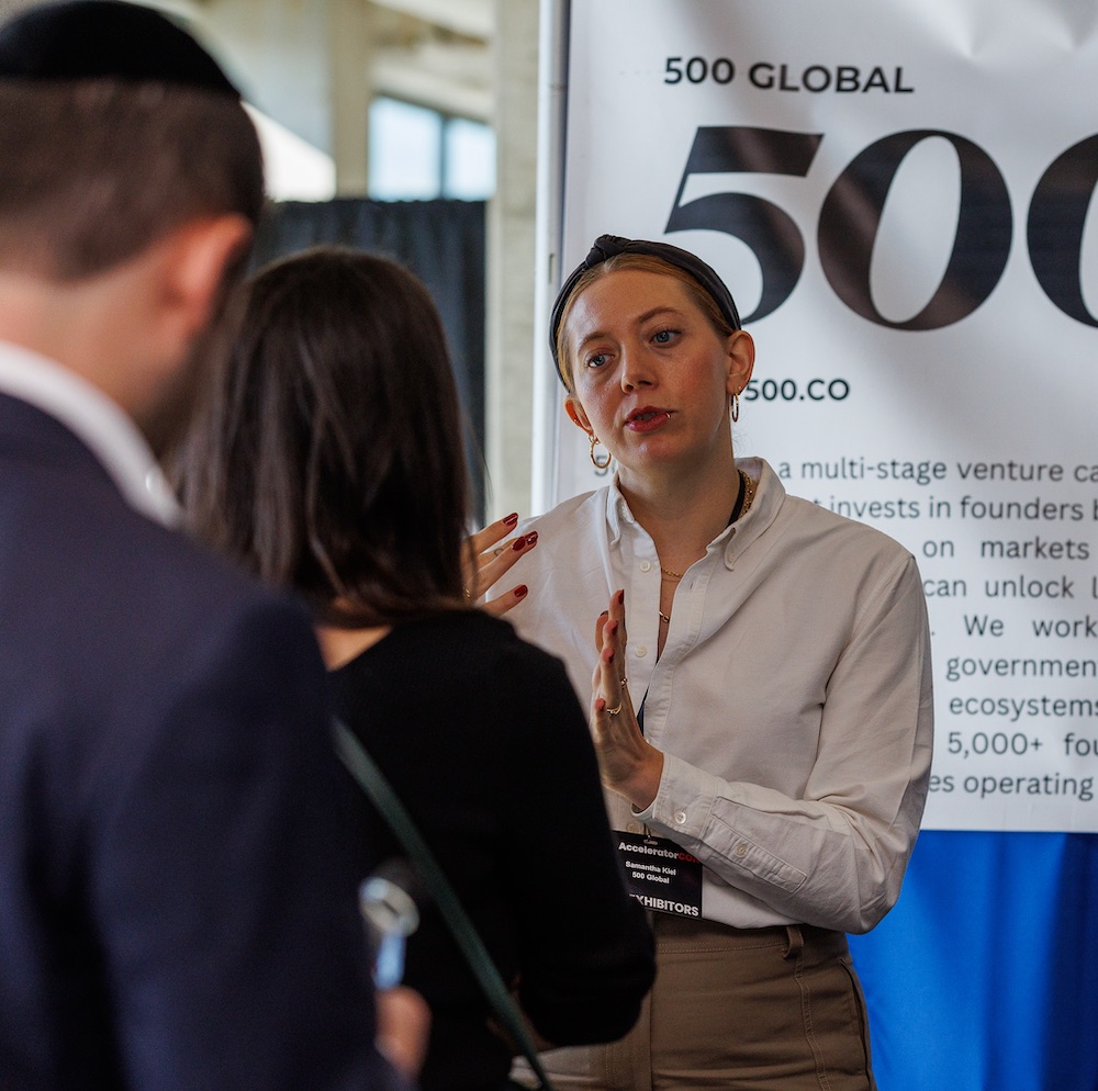 An AcceleratorCON exhibitor from 500 Global speaks with attendees