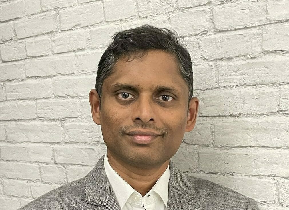 ACCELQ founder Mahendra Alladi in a gray jacket against a white brick wall