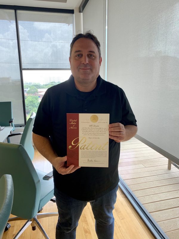 Achi Rotem standing in an office holding K2view’s U.S. patent certificate