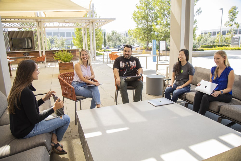 Five people seated with laptops in an outdoor meeting area in a photo from Acorns’ About page