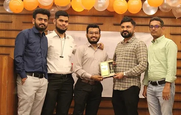 Five Acquaint Softtech team members posing with a plaque beneath balloons at a company event