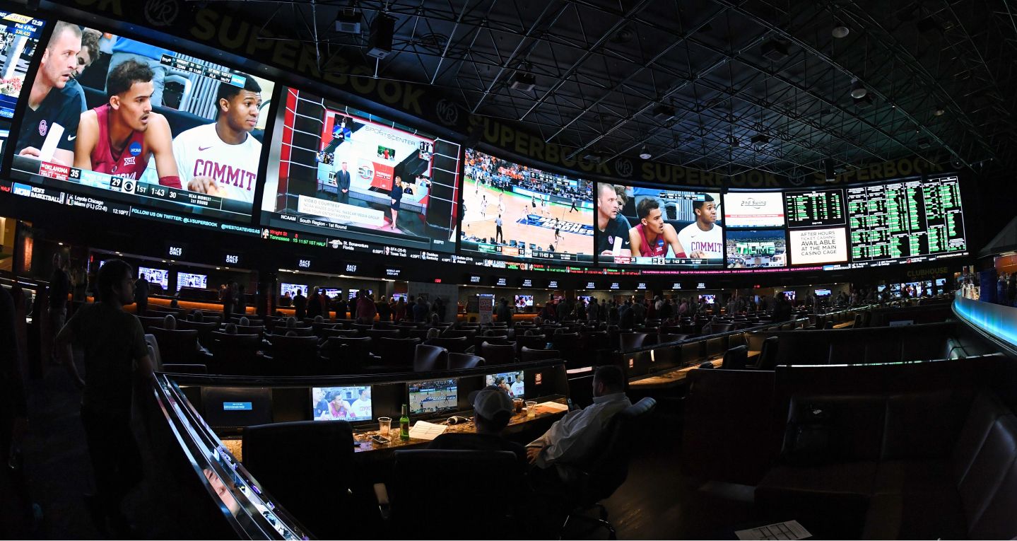 A sportsbook viewing room filled with large game screens and odds boards