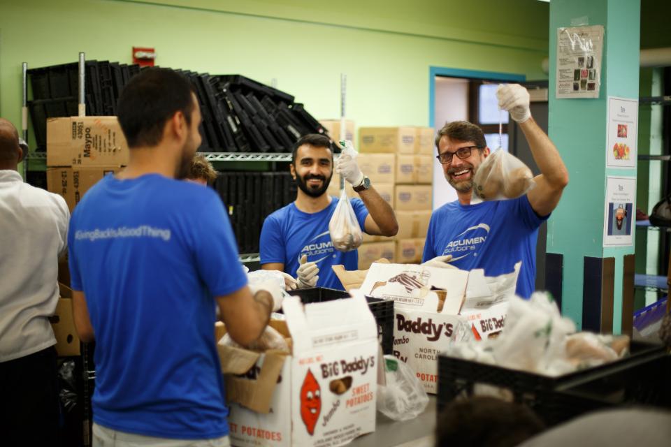 Acumen Solutions employees in blue shirts packing sweet potatoes during a New York volunteering event