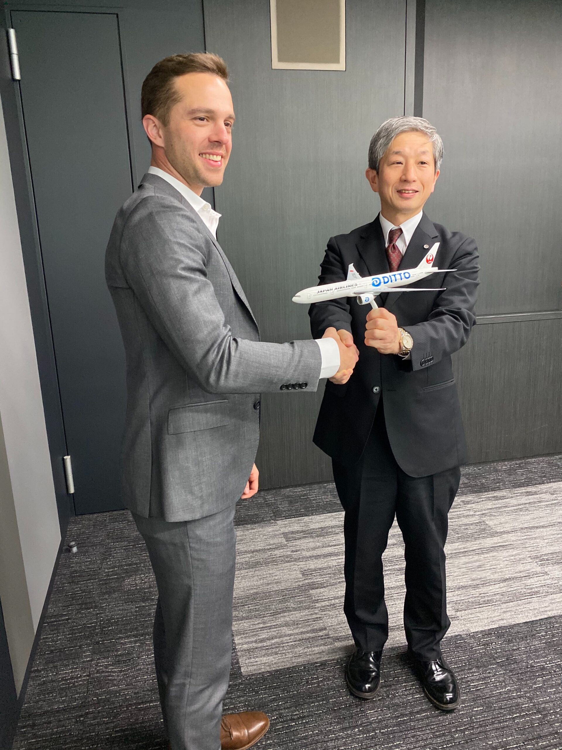 Adam Fish shaking hands with a Japan Airlines executive holding a Ditto-branded model airplane