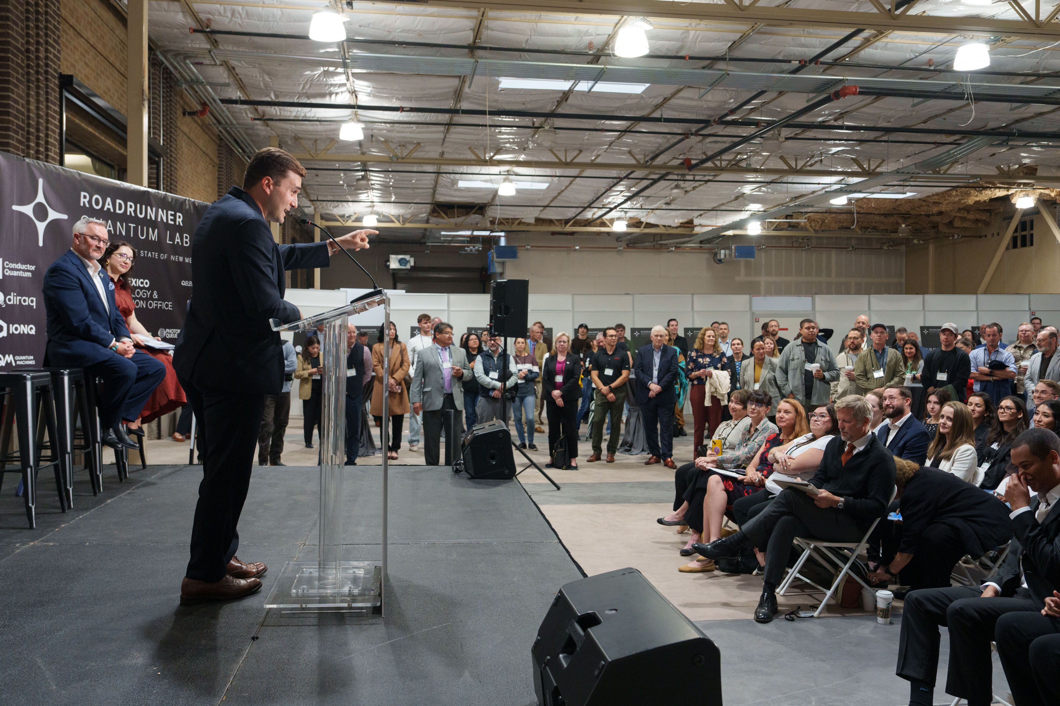 Adam Hammer speaking at a lectern to an audience at the Roadrunner Quantum Lab opening