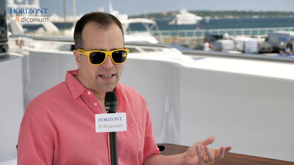 Adam Helfgott wearing yellow sunglasses and a pink shirt while being interviewed at Cannes