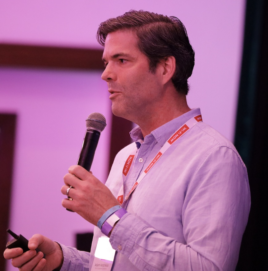 Adam Hotchkiss holding a microphone and presentation remote at Wi-Fi World Congress Americas