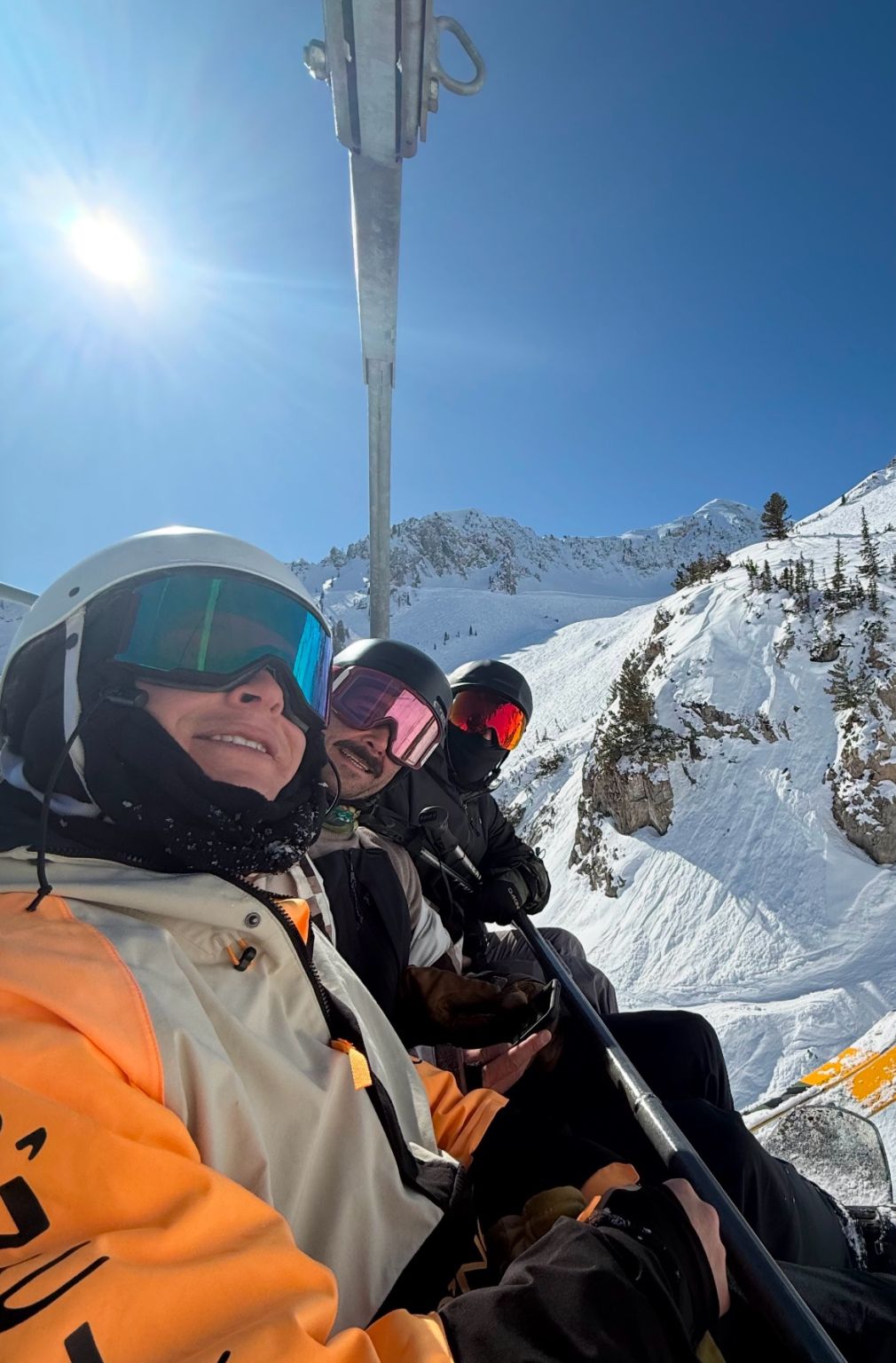 Adam Lebowitz and friends riding a ski lift at Powder Mountain under a bright blue sky