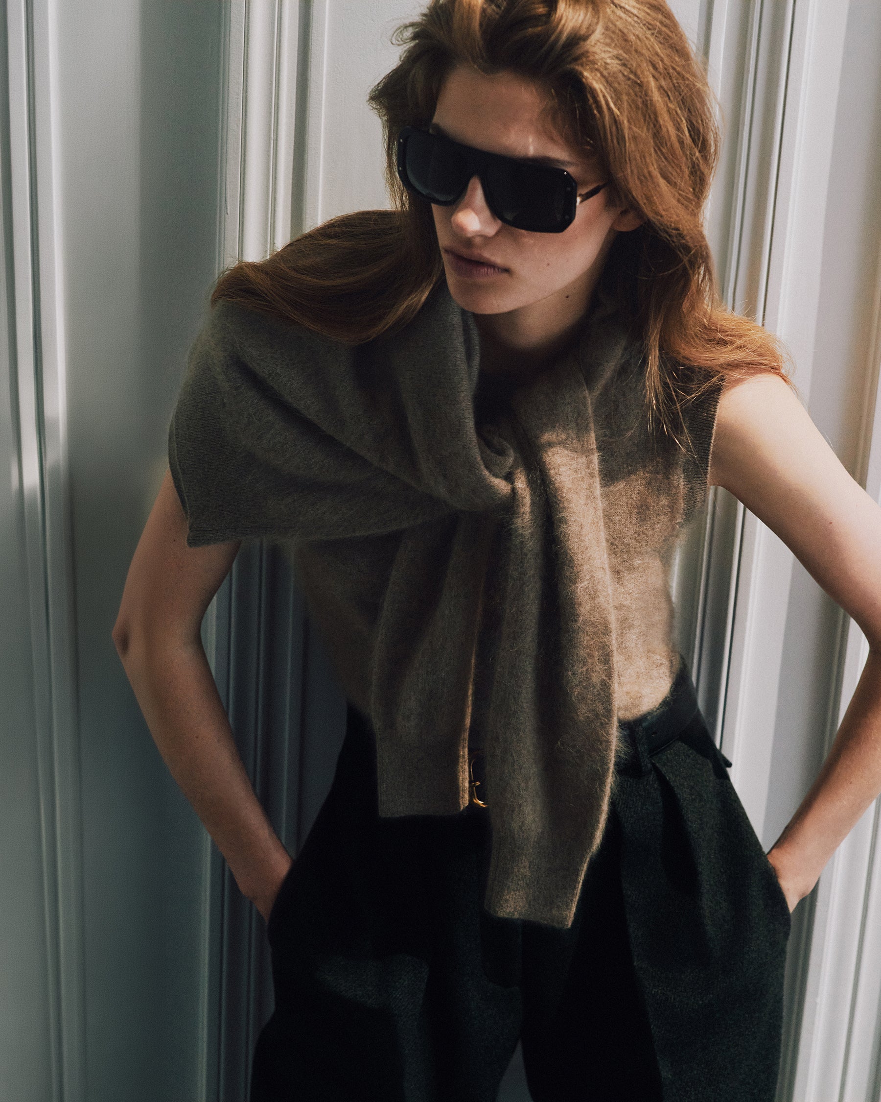 Model wearing a soft neutral knit draped over her shoulders with tailored dark trousers