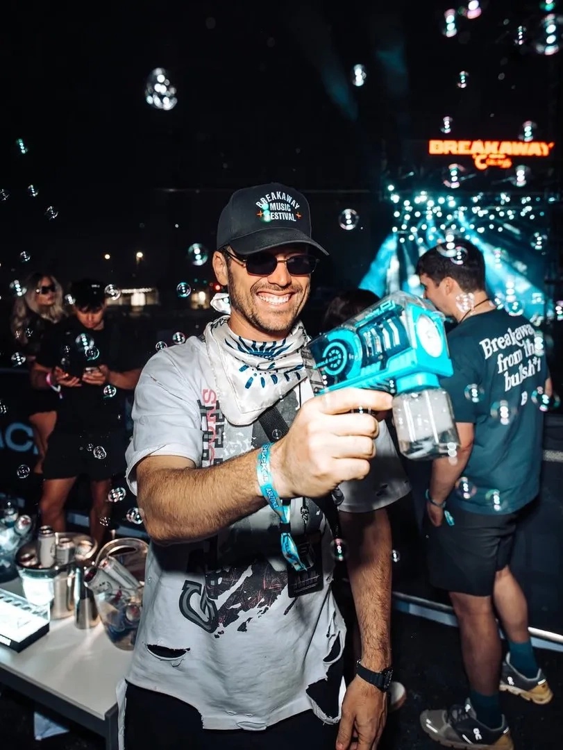 Adam Lynn smiles in a Breakaway cap while holding a bubble machine at an event.