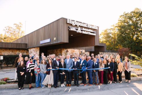 Community members and leaders gather behind a blue ribbon outside the newly branded Highpoint Health Sewanee building