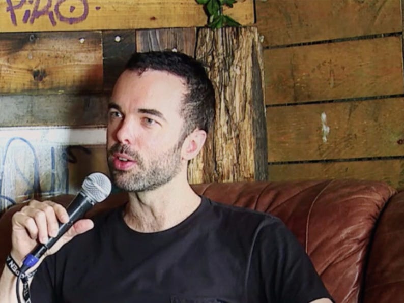 Adam Smith holding a microphone while seated on a leather couch
