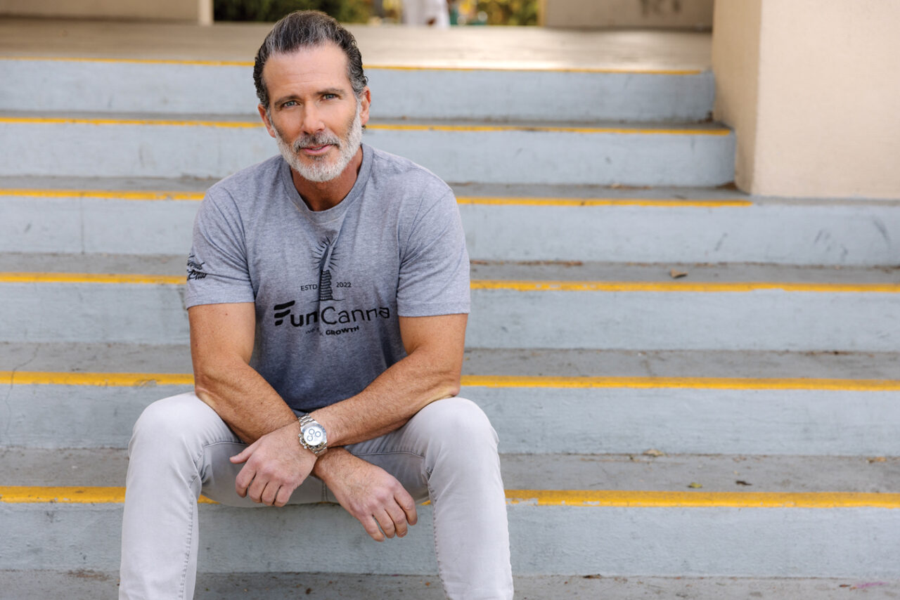 Adam Stettner seated on outdoor steps wearing a FundCanna shirt