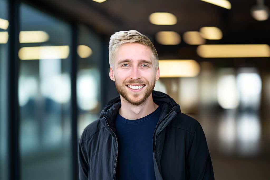 Adam Turner smiling in a dark jacket in an indoor workspace