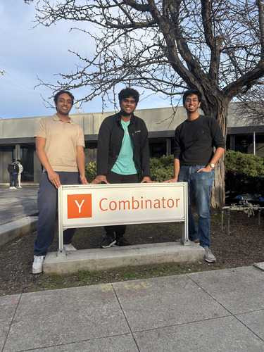 Adarsh Ambati, Ansh Gupta, and Aditya Iyengar standing behind a Y Combinator sign outdoors