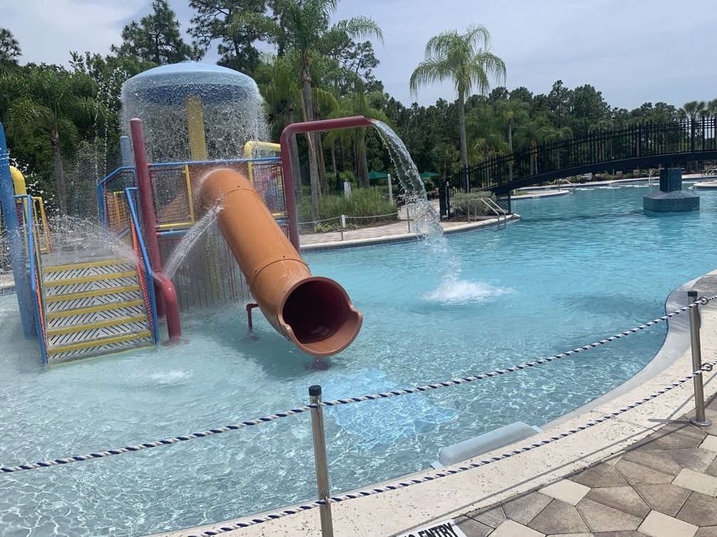 A commercial swimming pool with an orange slide and water play equipment, shown on Vermana’s website