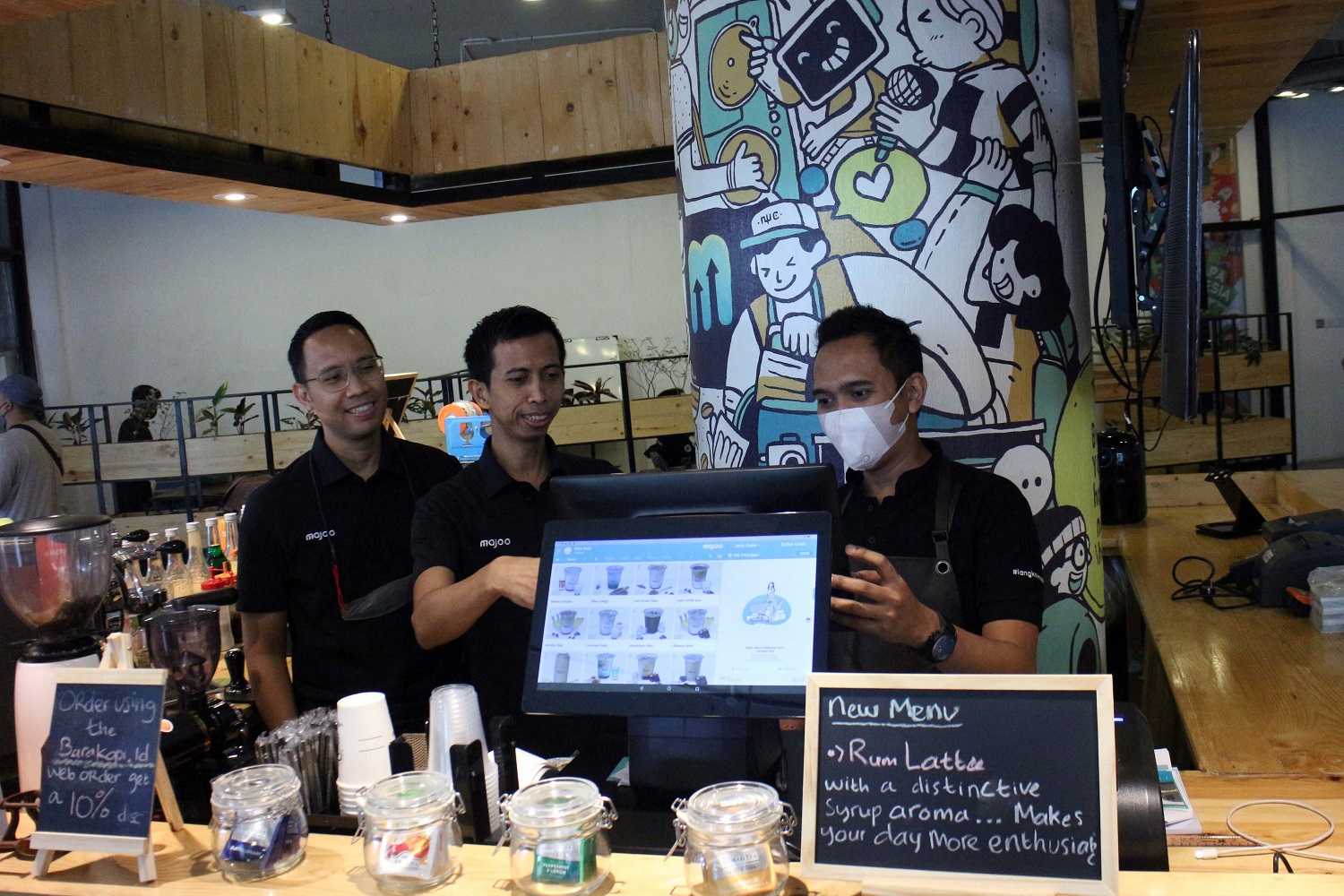 Adi Wahyu Rahadi, center, and Audia Rizal Harahap, left, discussing a point-of-sale system with a merchant at a café counter