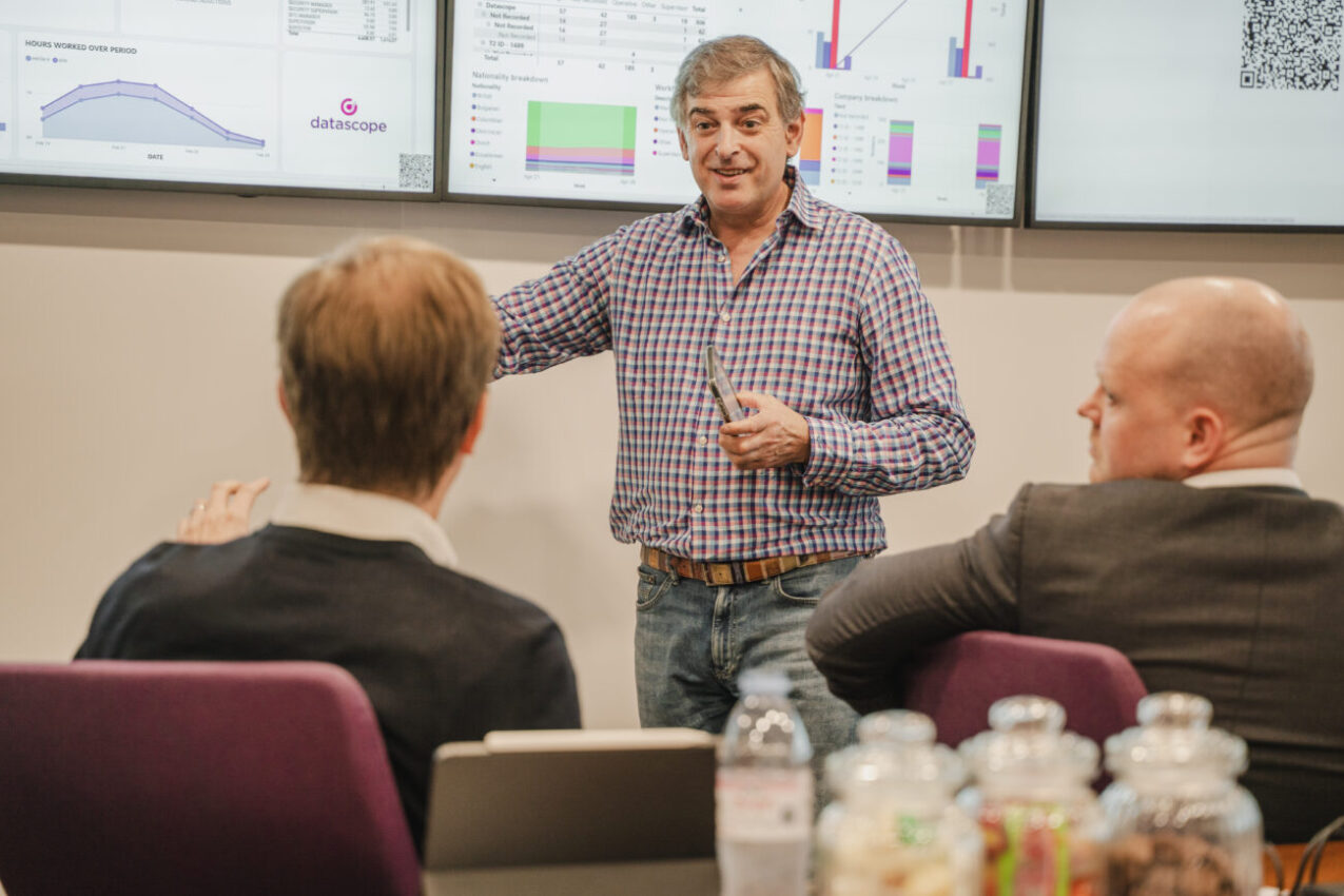 Adrian Butt presenting to customers, with DataScope dashboards displayed behind him