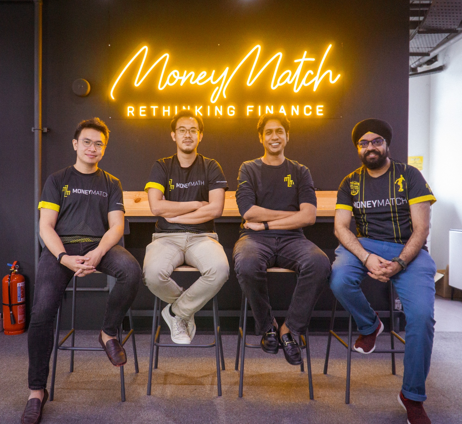 MoneyMatch leadership seated together beneath the company's yellow office sign