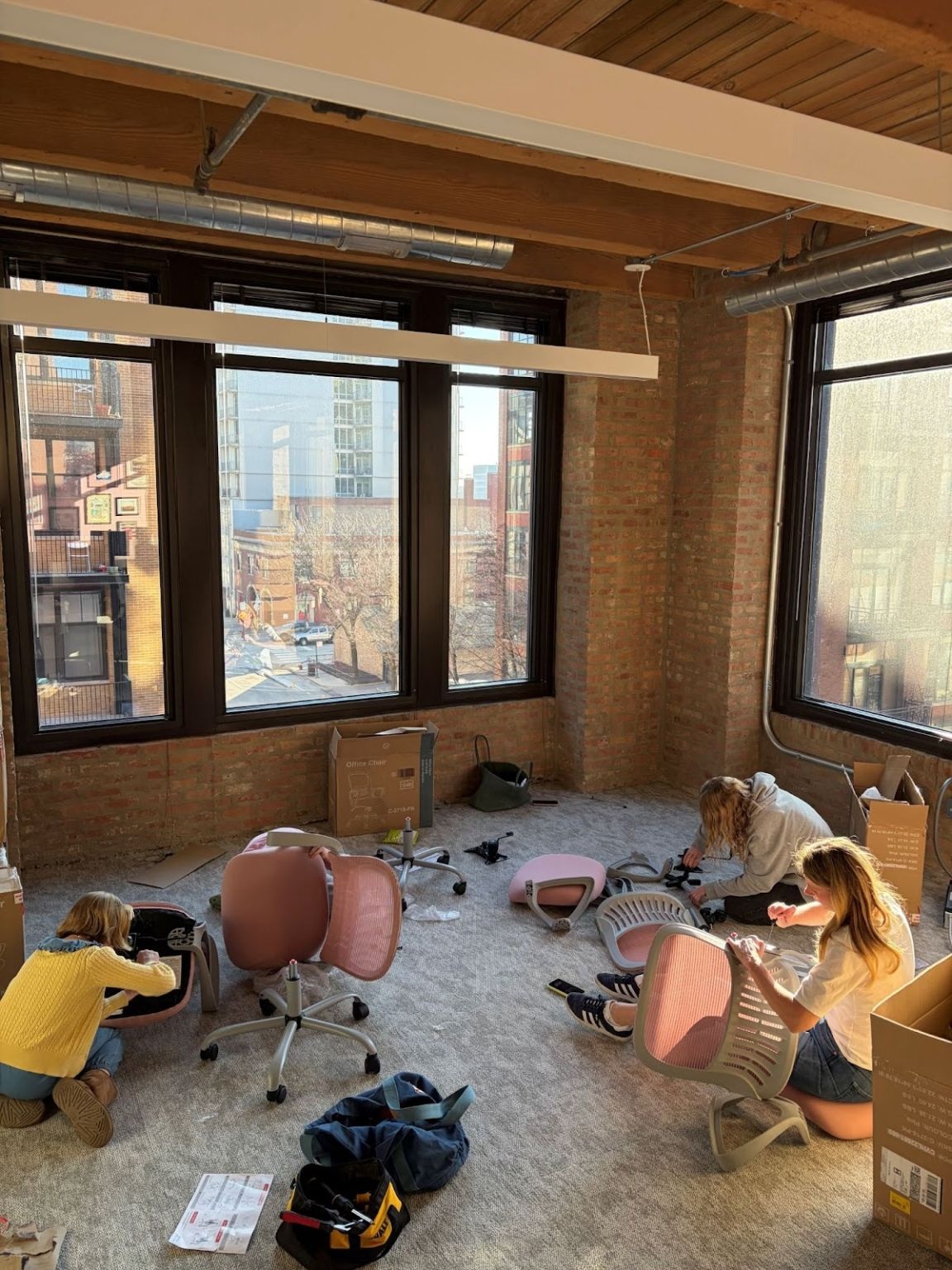 Family members assembling pink office chairs amid boxes in Skirt PR’s new brick-and-timber office