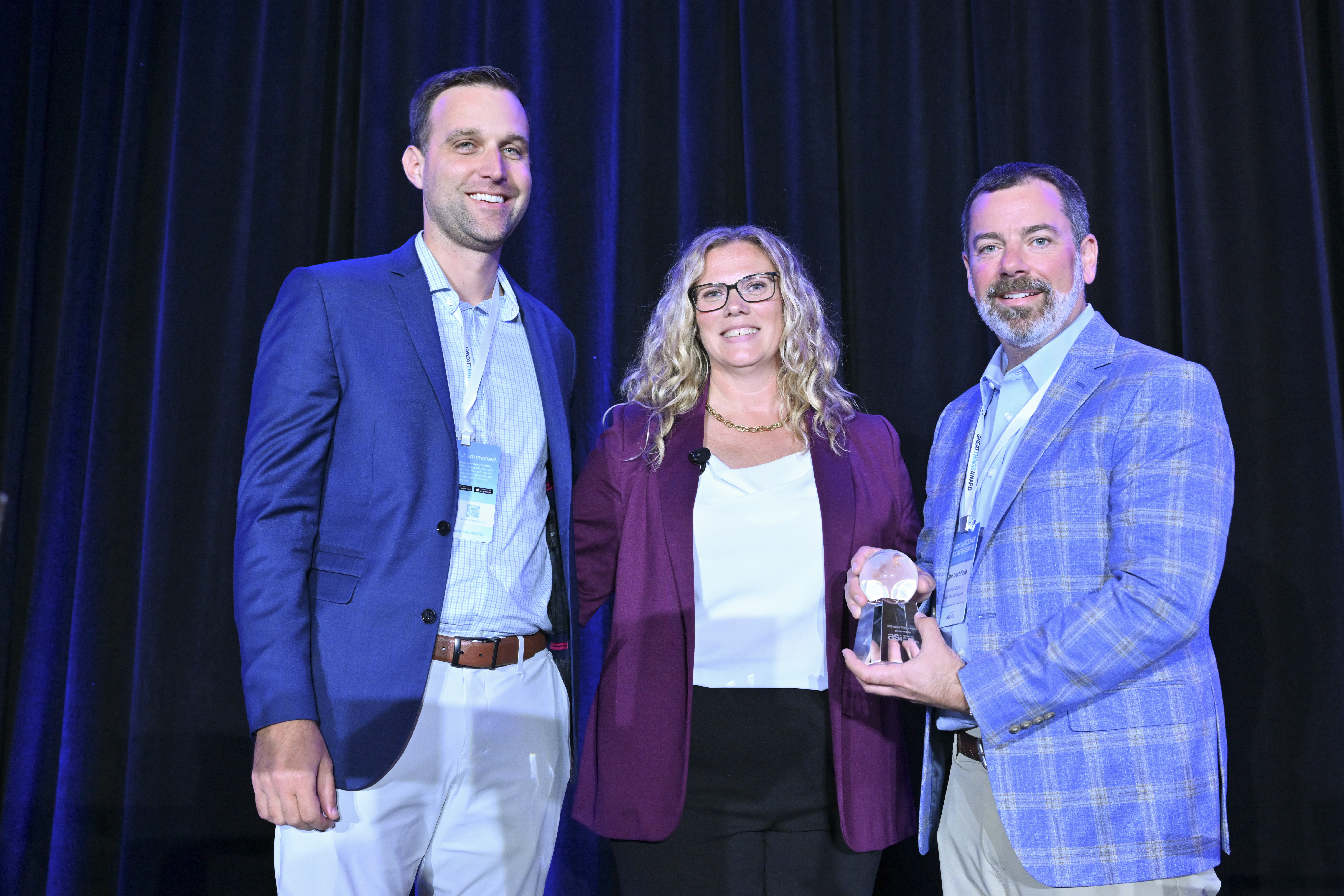 Three people posing with a Great Things Award trophy at an ASI event